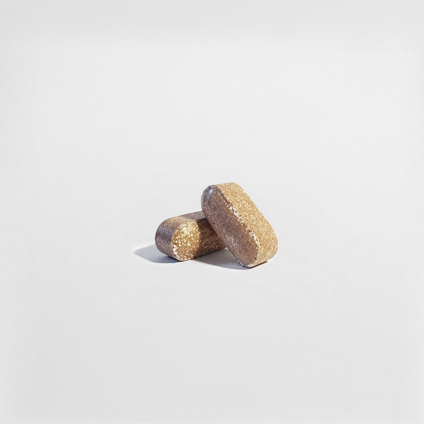 Close-up of two brown Men's Vitality Tablets showcasing their natural formulation for energy and stamina enhancement.